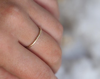 Puede incluir: Un delicado anillo de oro con una superficie texturizada. El anillo es delgado y parece hecho a mano. El anillo se lleva en un dedo, mostrando su simple elegancia. El diseño del anillo es minimalista y adecuado para el uso diario.
