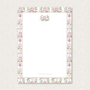 May include: A white stationery sheet with a pink floral border and a matching floral accent at the top. The border features pink roses and green leaves. The text "VICTORIA KING" is printed at the bottom.