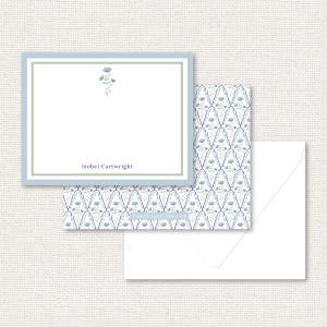 Puede incluir: Juego de papelería con un diseño floral en azul claro y verde. El juego incluye un bloc de notas con borde azul, una tarjeta estampada y un sobre blanco. El bloc de notas tiene el nombre "Isobel Cartwright" impreso.