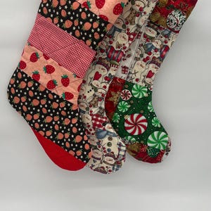 以下が含まれることがあります： 様々な模様のクリスマスストッキングのコレクション。イチゴがピンクと黒の背景に描かれたもの、雪だるまが描かれたもの、キャンディケーンとオーナメントのデザインのものがあります。各ストッキングには赤い袖口と吊り下げ用のループが付いています。