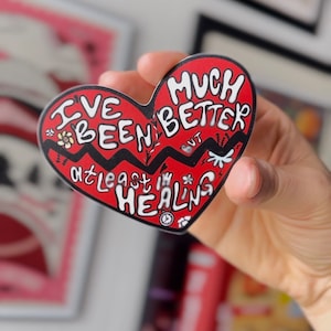 May include: Red heart-shaped sticker with black outline and white text that reads "I've been better but at least I'm healing" with a flower and lightning bolt graphic.