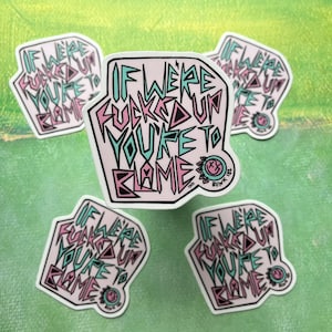 Op de afbeelding: Vijf roze en blauwe stickers met de tekst "If we're fucked up you're to blame" in een vet, gestileerd lettertype. De stickers bevinden zich op een groene achtergrond.