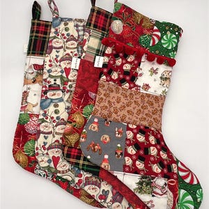 May include: Four Christmas stockings with various festive patterns. Designs include snowmen, dogs in hats, gingerbread men, plaid, and candy canes. Each stocking has a loop for hanging and is made of fabric.