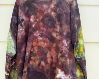 May include: A crew neck sweatshirt with a tie-dye pattern in shades of brown, purple, and green. The long sleeves have a splash of green and yellow. The garment is hanging on a black hanger against a light-colored background.