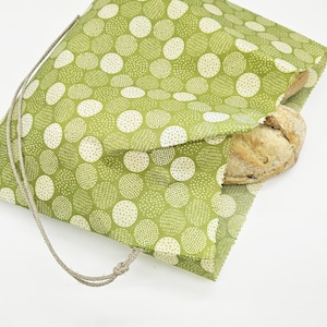Peut inclure: Un sac à pain vert à pois blancs contenant une miche de pain. Le sac en tissu est orné d'un motif à pois et se ferme avec un cordon. Le pain est partiellement visible.