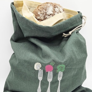 Könnte beinhalten: Eine dunkelgrüne Brotbeutel mit gestickten Gabeldesigns, die ein Brot enthalten. Die Tasche hat ein beiges Innenfutter und einen Kordelzugverschluss. Die gestickten Gabeln haben Gemüse darauf.