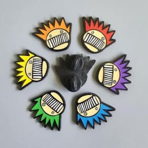 May include: A set of colourful enamel pins with a comb design and a black pin. The pins have orange, red, yellow, green, purple, and blue accents. The pins glow in the dark.