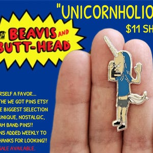May include: A silver enamel pin featuring a cartoon character from the animated series "Beavis and Butt-Head". The character is wearing a blue shirt and has a unicorn horn on his head. The pin is on a finger and the text "UNICORNHOLIO" PIN is visible above the pin.