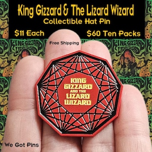 Puede incluir: Un pin para sombrero octogonal rojo y negro con las palabras "King Gizzard and the Lizard Wizard" en letras doradas. El pin presenta un diseño geométrico con un contorno negro y un centro rojo.