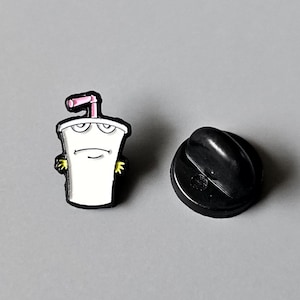May include: A white enamel pin of a cartoon character, a cup with a straw, with a black and white face and yellow arms. The pin is attached to a black metal backing.