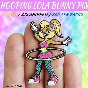 May include: A colorful enamel pin featuring Lola Bunny from Looney Tunes, hula hooping. The pin has a gold outline and depicts Lola in a pink and blue outfit with a matching headband. Text on the pin reads "HOOPING LOLA BUNNY PIN" and "WE GOT PINS."