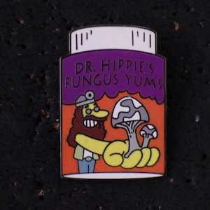 Könnte beinhalten: Ein farbenfroher Emaille-Pin mit einem Cartoon-Bild eines Arztes, der Pilze hält. Der Pin trägt die Aufschrift "DR. HIPPIE'S FUNGUS YUMS" in lila Schrift. Der Pin hat eine weiße Oberseite und ist vor einem dunklen Hintergrund platziert.