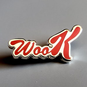 May include: A silver-colored pin with the word "Wook" in red lettering. The letters are stylized and have a 3D effect.