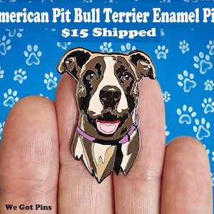 May include: An enamel pin featuring an American Pit Bull Terrier. The pin depicts the dog's head with a black, white, and brown color scheme, a pink tongue, and a purple collar. The background is blue with white paw prints, and the text "American Pit Bull Terrier Enamel Pin" is at the top.