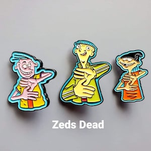 Op de afbeelding: Drie emaille pins met stripfiguren uit Ed, Edd n Eddy, die elk een handgebaar maken. De figuren dragen gele, groene en oranje shirts. De tekst Zeds Dead staat in witte, vetgedrukte letters onder de pins gedrukt.