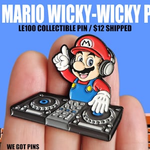 Puede incluir: Un colorido pin de esmalte con un personaje de dibujos animados que lleva un sombrero rojo y auriculares, con un gesto de pulgar hacia arriba. El personaje está posicionado sobre una mesa de mezclas de DJ. El texto "DJ MARIO WICKY-WICKY PIN" se muestra arriba.