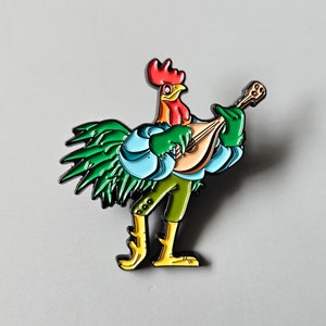 Può includere: Uno spillo smaltato con un gallo che suona un liuto. Il gallo indossa una camicia blu e pantaloni verdi. Lo spillo è verde, blu e giallo.