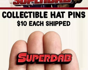 以下が含まれることがあります： 黒い縁取りのある赤いエナメルピンに「SUPERDAB」の文字が書かれています。ピンは手で持たれています。