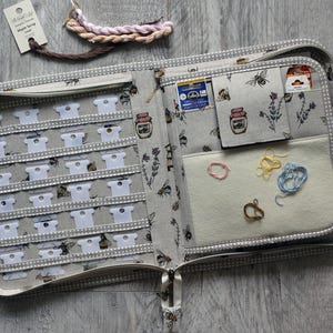 May include: A grey fabric organiser case with a bee and honey jar print, featuring rows of white plastic thread bobbins, a felt needle pad with loose embroidery floss, and a small pocket. The case has a zip closure and polka dot trim.