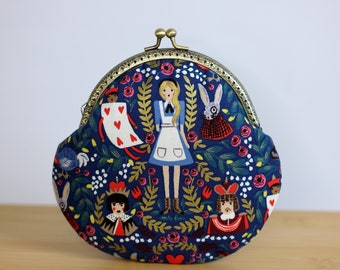 May include: A navy blue coin purse with a brass kiss-lock clasp featuring a printed pattern of Alice in Wonderland characters including a girl in a blue dress, a rabbit, a playing card, and royalty surrounded by red roses and green foliage.
