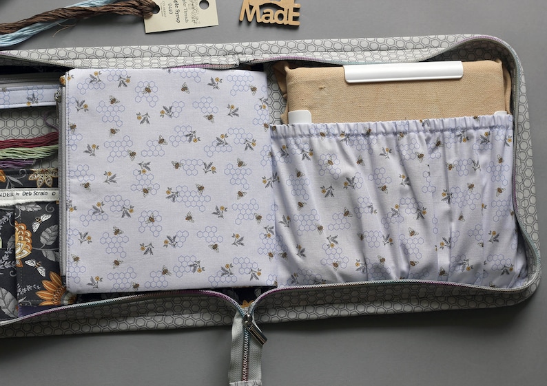 May include: Open grey fabric zippered pouch with a honeycomb and bee pattern lining. The pouch is filled with fabric scraps and a white plastic ruler. The pouch is labeled "Made".