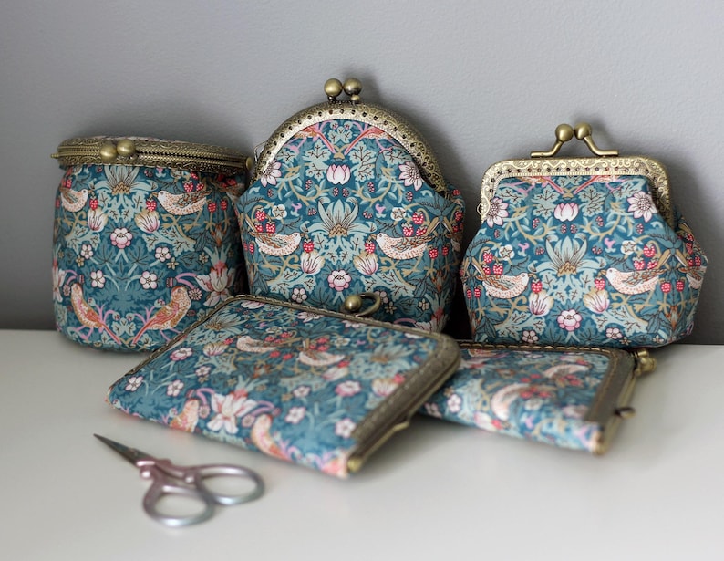 May include: A collection of five fabric pouches and purses featuring a teal floral and bird pattern with antique brass-toned metal kiss-lock clasps. The set includes various shapes and sizes, accompanied by a small pair of metal scissors.