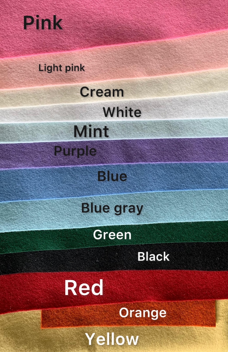 May include: A collection of felt fabric sheets arranged in horizontal layers, featuring colors labeled as Pink, Light pink, Cream, White, Mint, Purple, Blue, Blue gray, Green, Black, Red, Orange, and Yellow. Each strip displays a soft, matte texture.