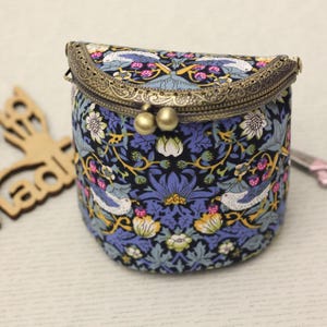 May include: A small, round, fabric purse with a decorative metal clasp. The purse features a blue and black floral pattern with birds and flowers. The clasp is a bronze color, and the purse has a vintage aesthetic.