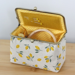 May include: A yellow and white fabric coin purse with a lemon print. The purse is open and has a yellow felt lining with a few pins inside.