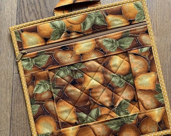 Pode incluir: Uma bolsa quadrada de tecido acolchoado com um padrão repetitivo de peras douradas e folhas verdes. A bolsa tem um fecho de correr superior com um puxador de metal, uma pequena alça de tecido no topo e uma borda de bolinhas amarelas e brancas.