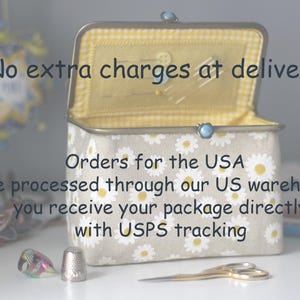 May include: A rectangular fabric sewing box with a beige exterior featuring a white daisy pattern. The interior is lined with yellow and white checkered fabric. A metal frame with a blue clasp secures the lid. A silver thimble and gold scissors.