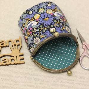 May include: A fabric pouch with a floral and bird pattern in shades of blue, yellow, and white, featuring a bronze-toned metal kiss-lock clasp and a teal interior lining with white polka dots, accompanied by wooden Hand Made text and scissors.