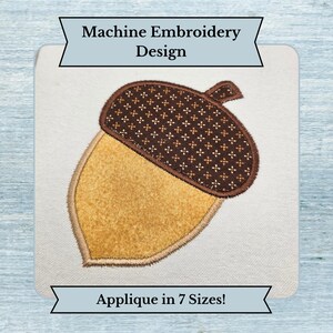 May include: A machine embroidery design of an acorn applique featuring a dark brown cap with a small repeating cross pattern and a textured golden-yellow nut. The text Machine Embroidery Design and Applique in 7 Sizes is visible.