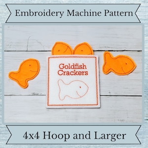 May include: Embroidery machine pattern for a box of Goldfish Crackers. The box is white with orange stitching and the text "Goldfish Crackers". There are four orange felt goldfish, three on top of the box and one to the right of the box.