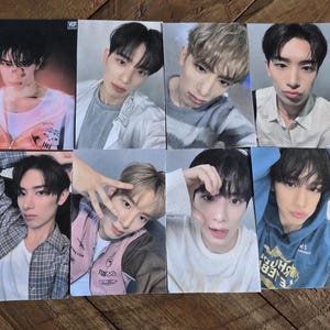 May include: Eight photo cards featuring young men in various poses. Each card shows a headshot or a pose of a man. The cards have a glossy finish and are arranged on a wooden surface.
