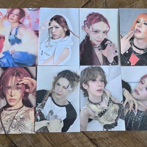 May include: A collection of eight photo cards featuring individuals with diverse hairstyles and makeup. The cards showcase various poses and outfits, with a range of colors and styles. The images are arranged on a wooden surface.