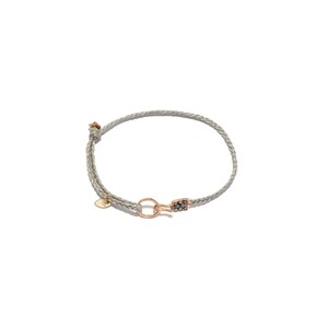 May include: A grey braided cord bracelet featuring a rose gold-toned circular clasp and a small, rectangular charm encrusted with tiny dark grey stones. A small, smooth, teardrop-shaped rose gold-toned metal tag hangs near the knot closure.