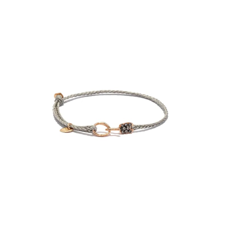 May include: A light grey braided cord bracelet featuring a circular gold-toned metal link, a small gold-toned circular charm, and a rectangular gold-toned metal component encrusted with small dark stones, secured with a sliding knot closure.