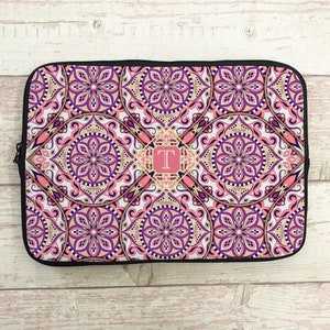 May include: A pink and purple laptop sleeve with a mandala pattern and a gold monogram "T" in the center.