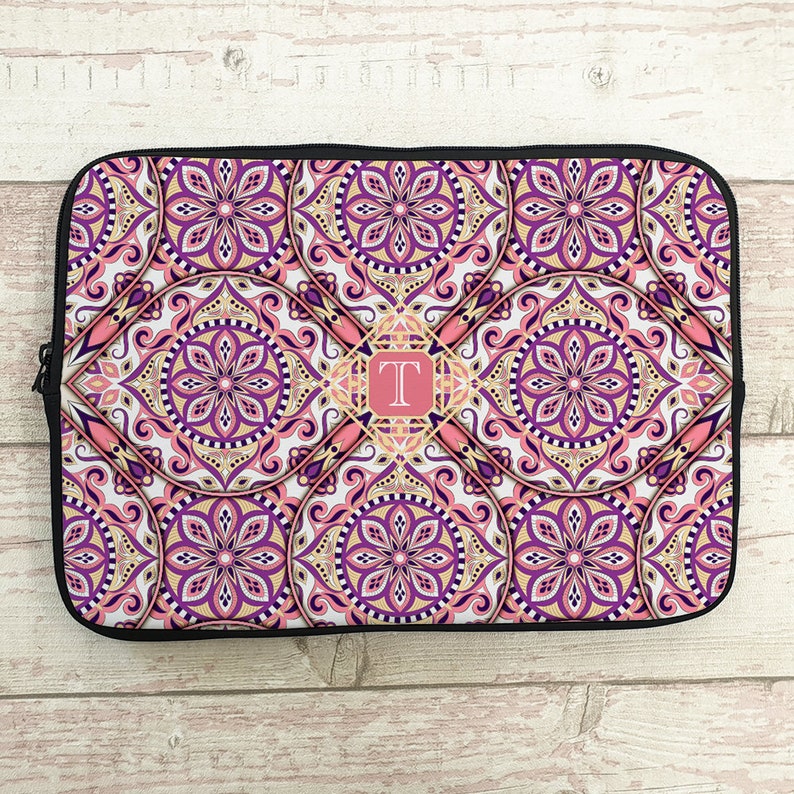 May include: A pink and purple laptop sleeve with a mandala pattern and a gold monogram "T" in the center.