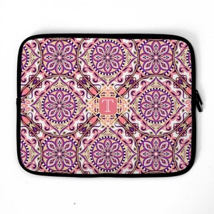 May include: A laptop sleeve with a pink, purple, and gold mandala pattern. The letter "T" is in the center of the design.