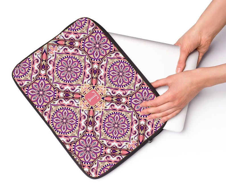 May include: A pink, purple, and gold laptop sleeve with a mandala pattern and a monogrammed initial "L" in the center.