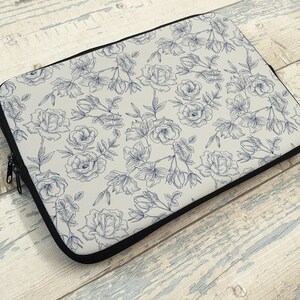 May include: A laptop sleeve with a white background and a blue floral pattern. The flowers are drawn in a delicate, vintage style.