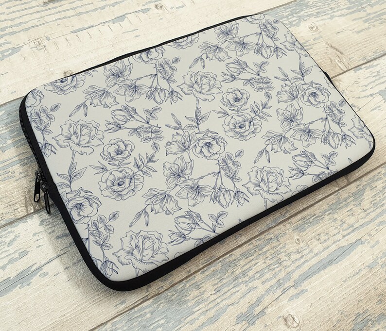May include: A laptop sleeve with a white background and a blue floral pattern. The flowers are drawn in a delicate, vintage style.