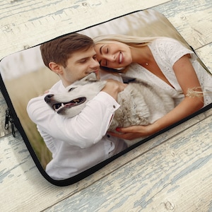 May include: A couple and their dog are hugging in a field. The couple is wearing white shirts and the dog is white and gray.
