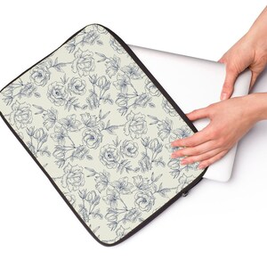 May include: A laptop sleeve with a cream background and a blue floral pattern. The sleeve is made of a soft, durable material and features a zipper closure.