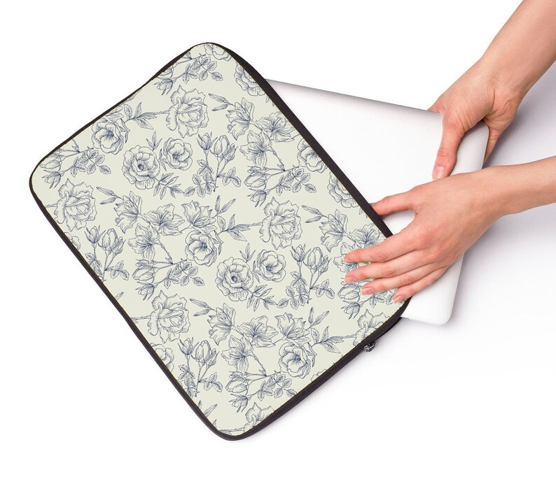 May include: A laptop sleeve with a cream background and a blue floral pattern. The sleeve is made of a soft, durable material and features a zipper closure.