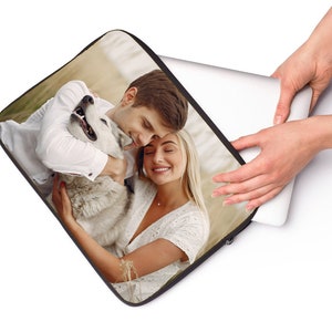 May include: A laptop sleeve with a photo of a couple hugging a dog. The couple is wearing white shirts and the dog is white and gray.