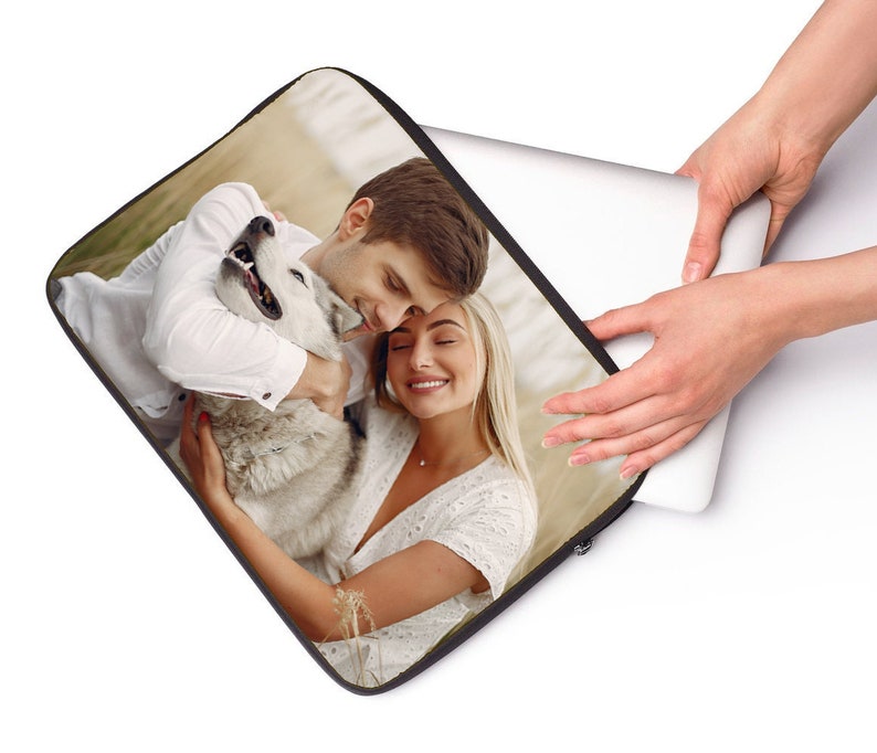 May include: A laptop sleeve with a photo of a couple hugging a dog. The couple is wearing white shirts and the dog is white and gray.