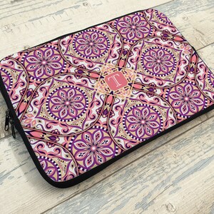May include: A pink and purple laptop sleeve with a mandala pattern and a gold monogram "T" in the center.